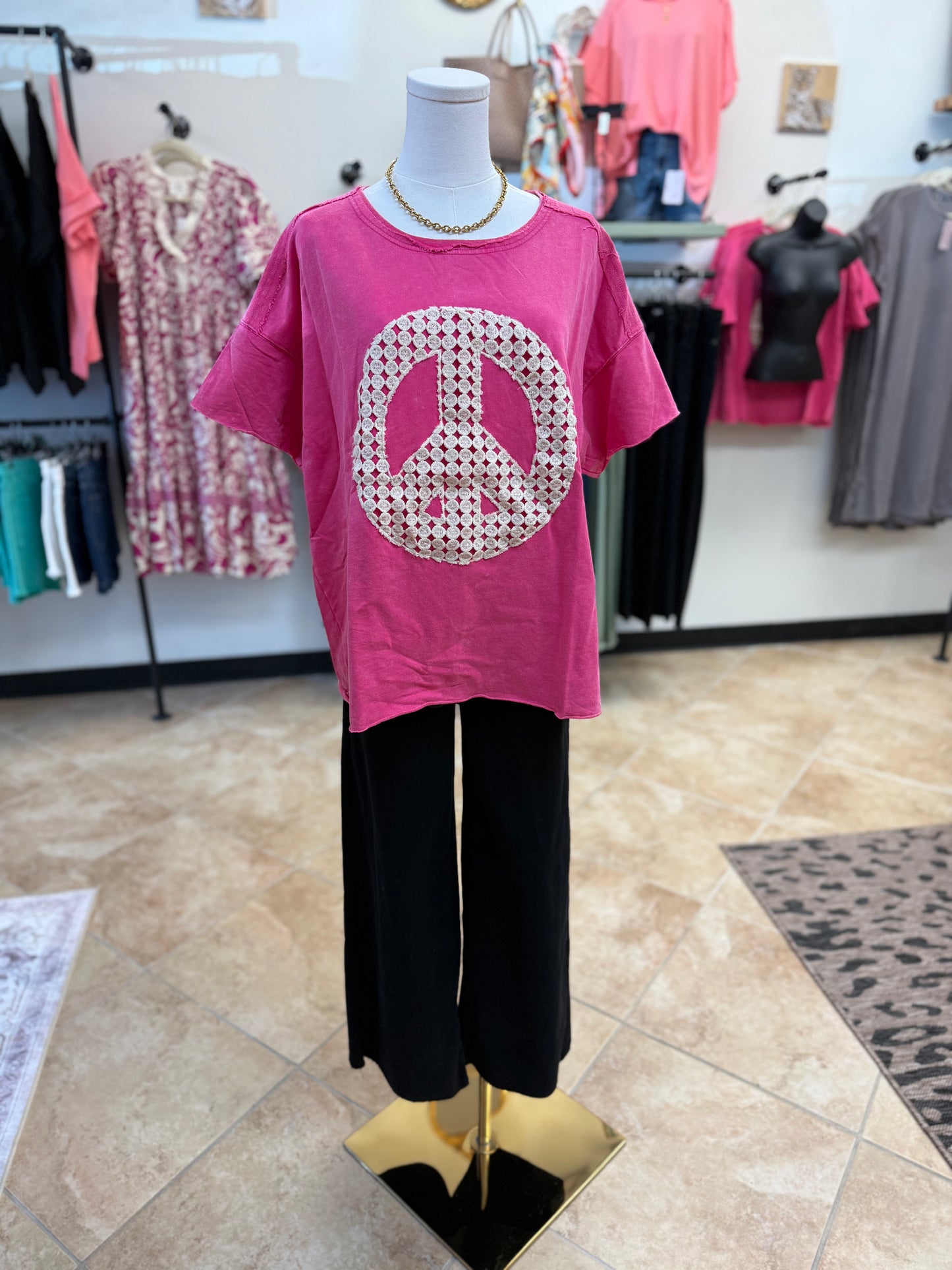 Mannequin wearing a pink t-shirt with a peace symbol design in a store setting.