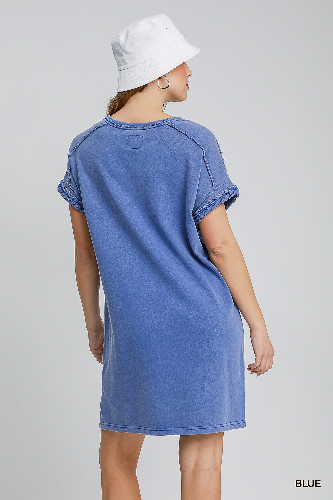 Woman wearing blue dress with braided sleeve detail on a white background