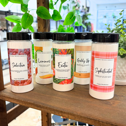 Five containers of different scented products on a wooden surface with plants in the background.