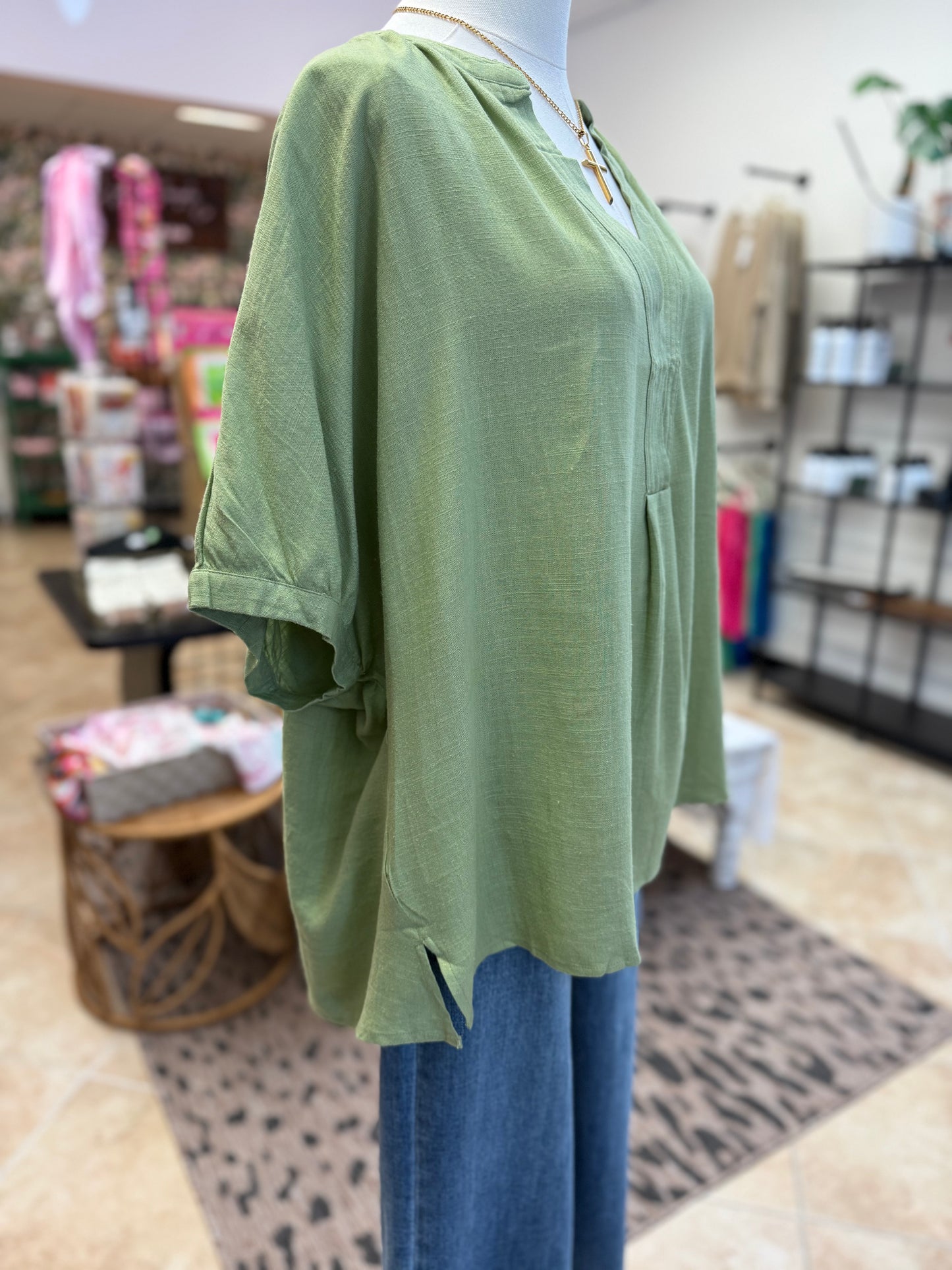 Green top on a mannequin with blue jeans in a store setting