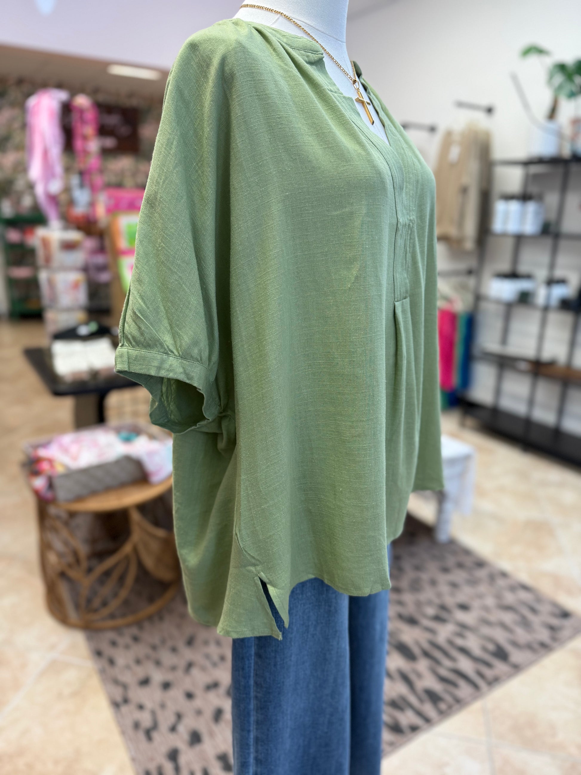 Green top on a mannequin with blue jeans in a store setting