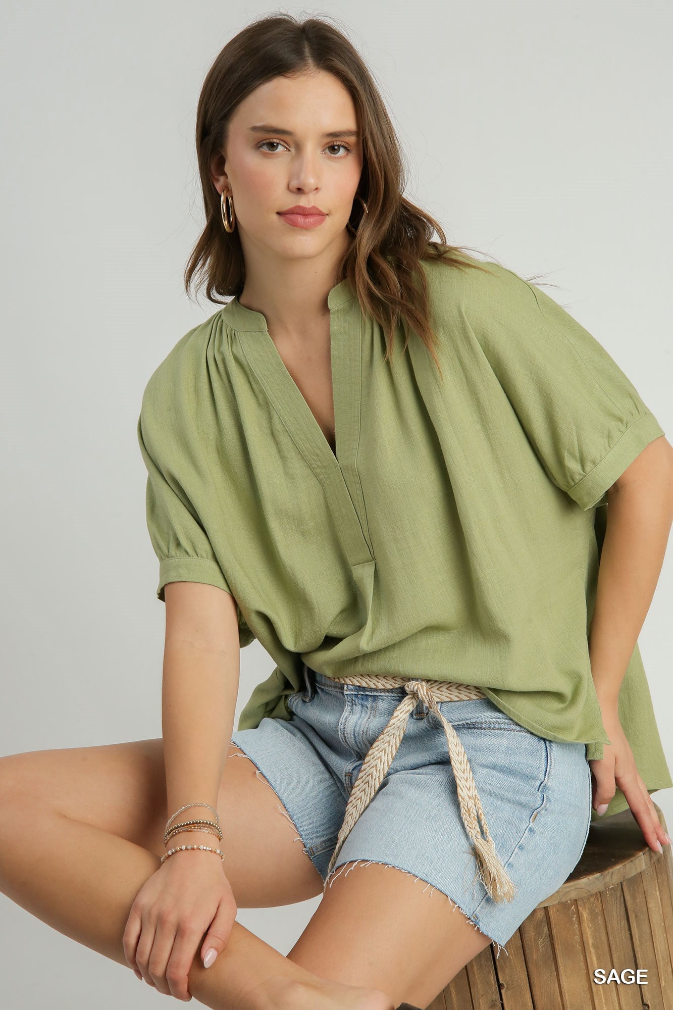 Woman wearing a green blouse and light blue shorts on a gray background