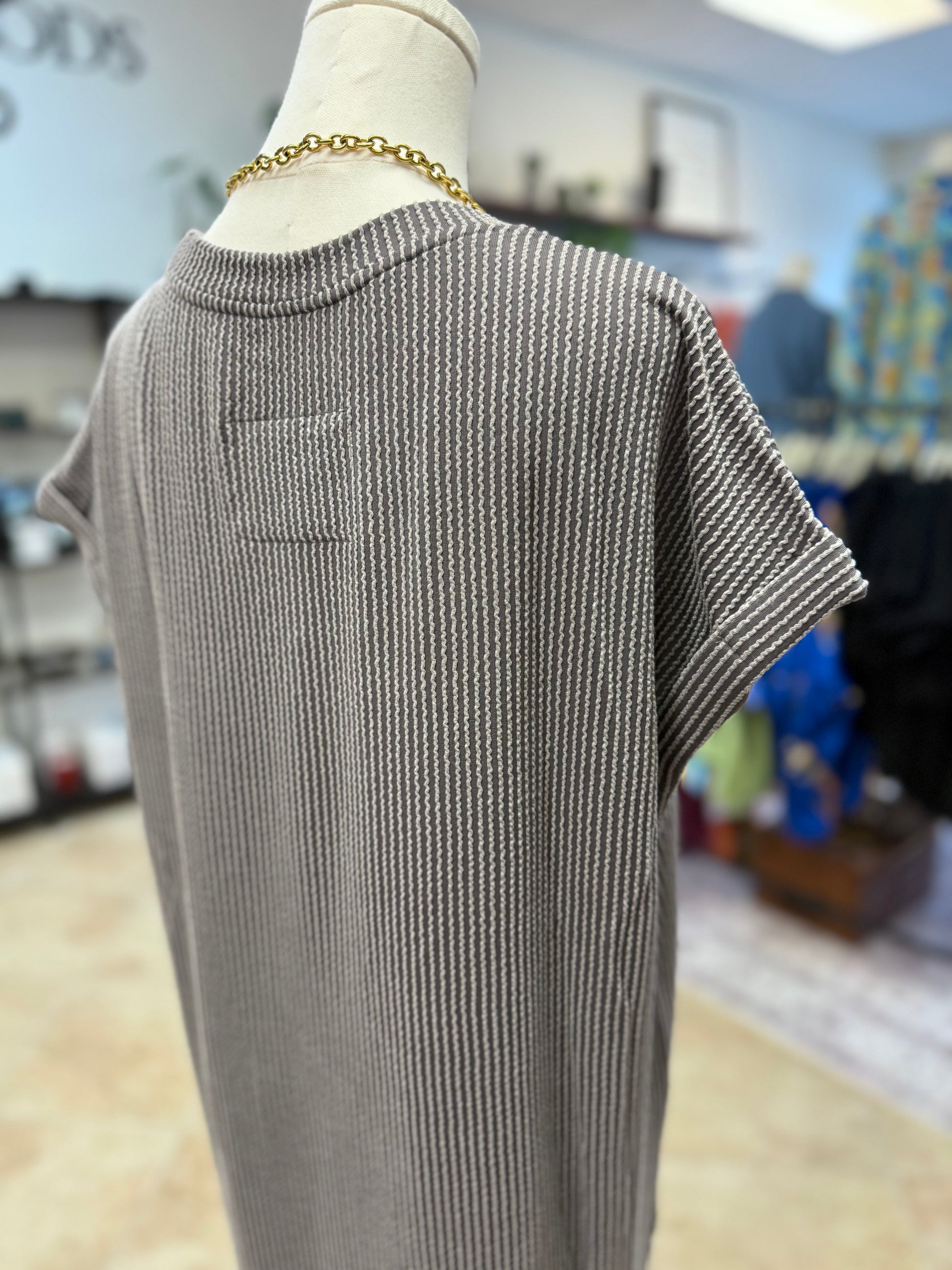 Mannequin wearing a gray ribbed dress with a blurred store interior background