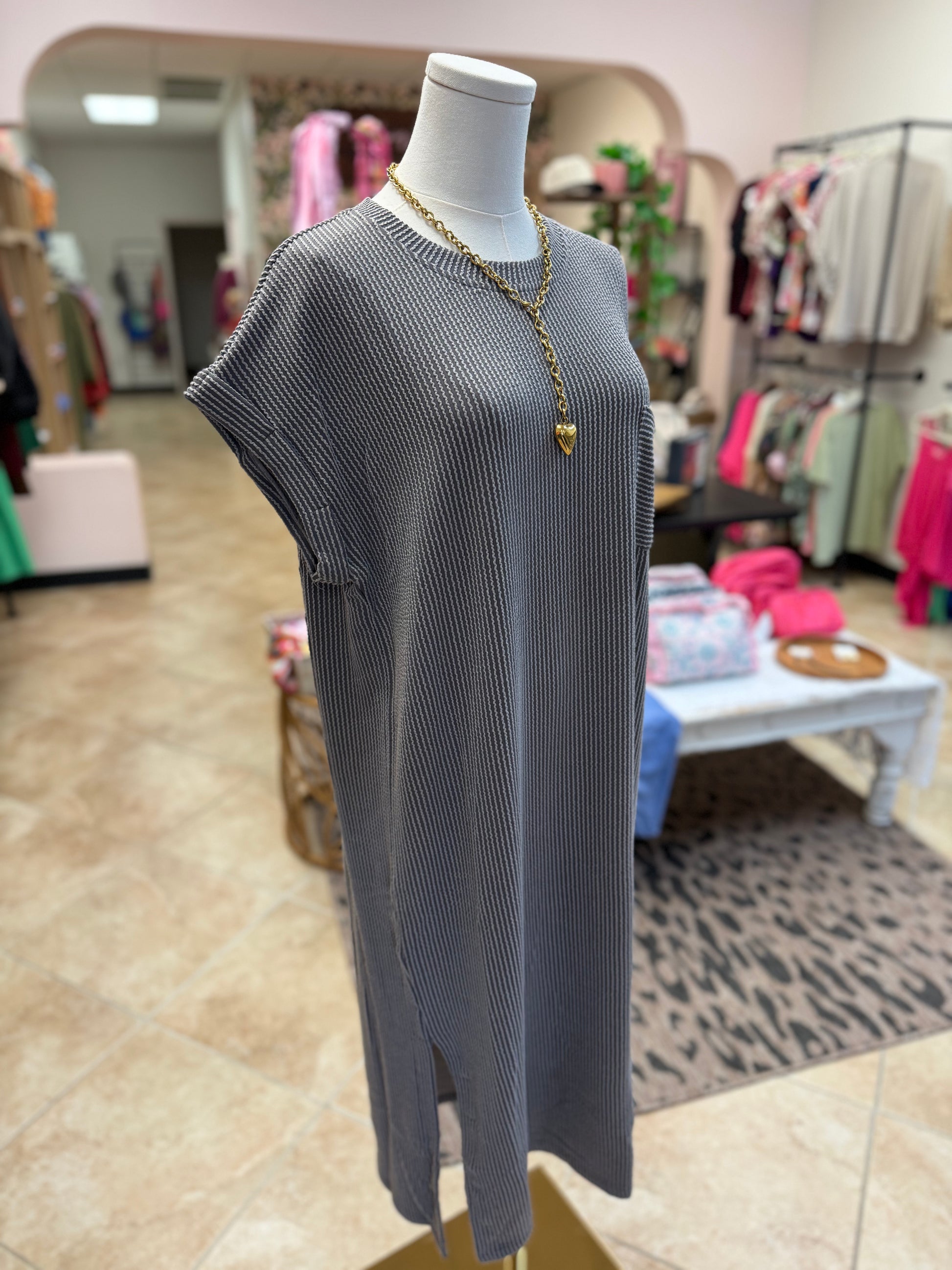 Gray ribbed dress on a mannequin in a store setting with clothing racks and displays in the background.