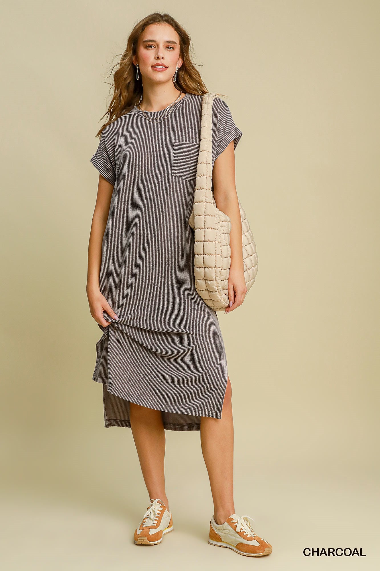 Woman wearing a gray dress holding a beige bag against a beige background