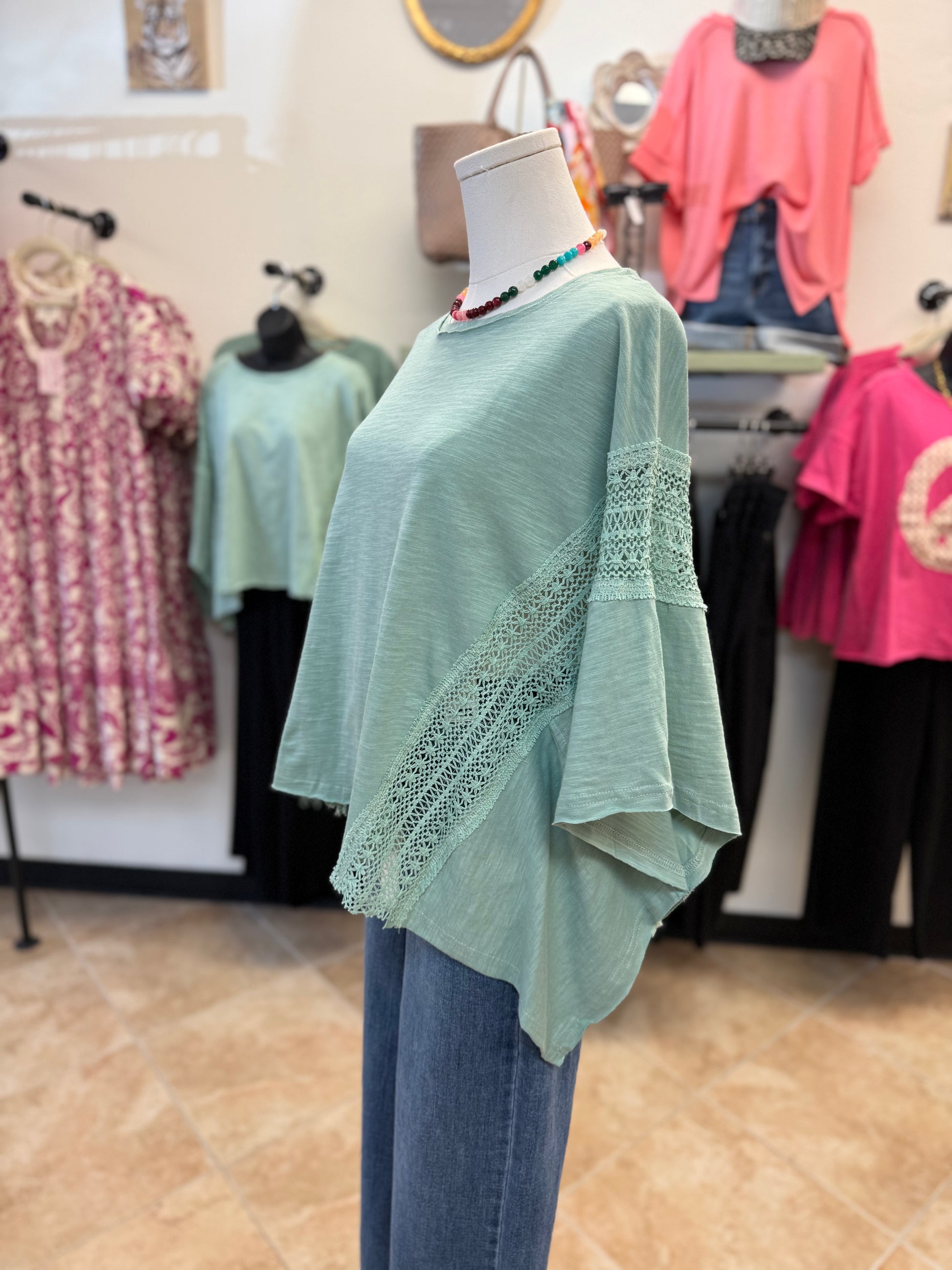 Mannequin wearing a light green poncho style blouse with lace details in a clothing store.