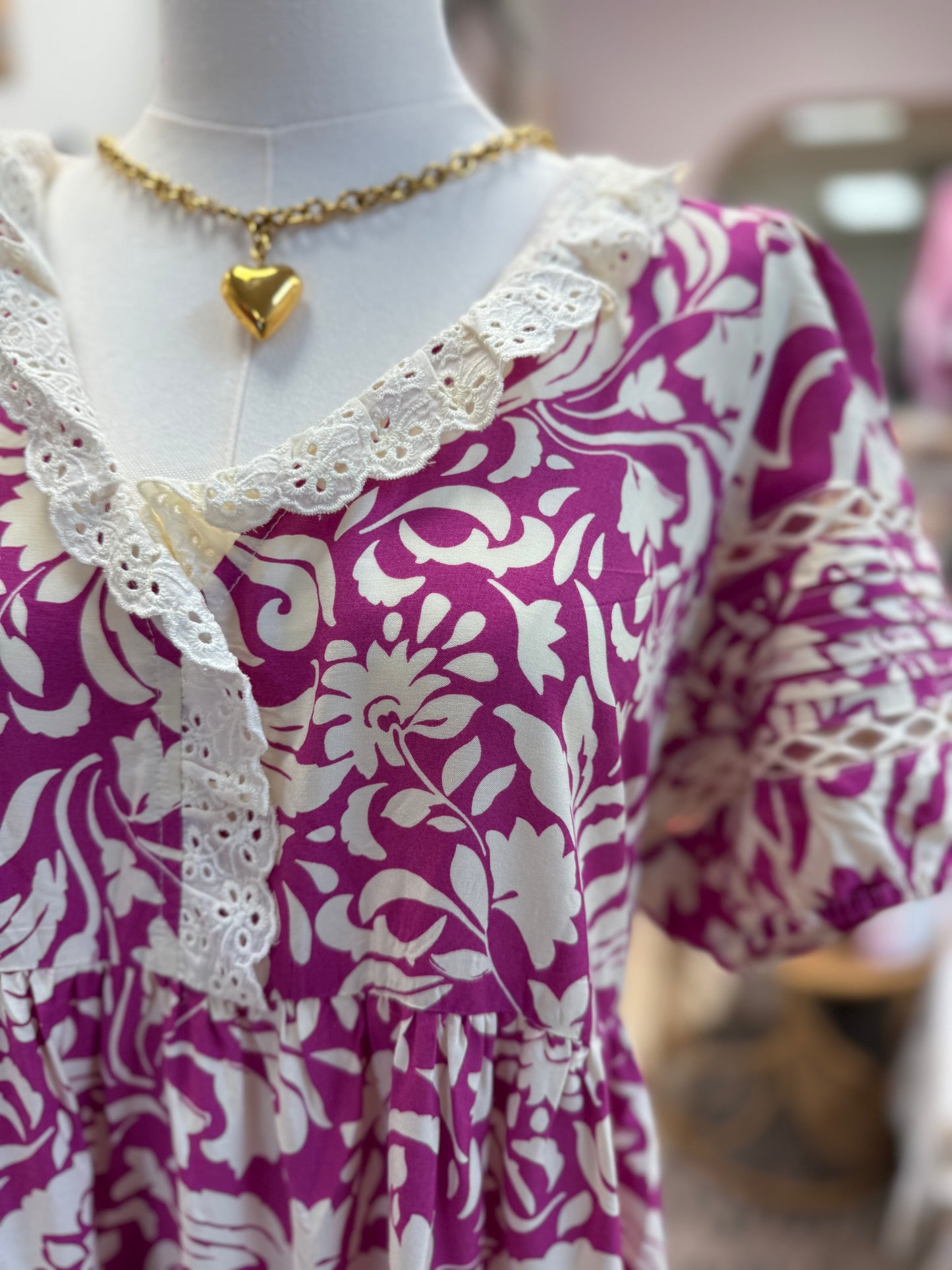 Mannequin wearing a pink floral dress with lace trim and a gold necklace.