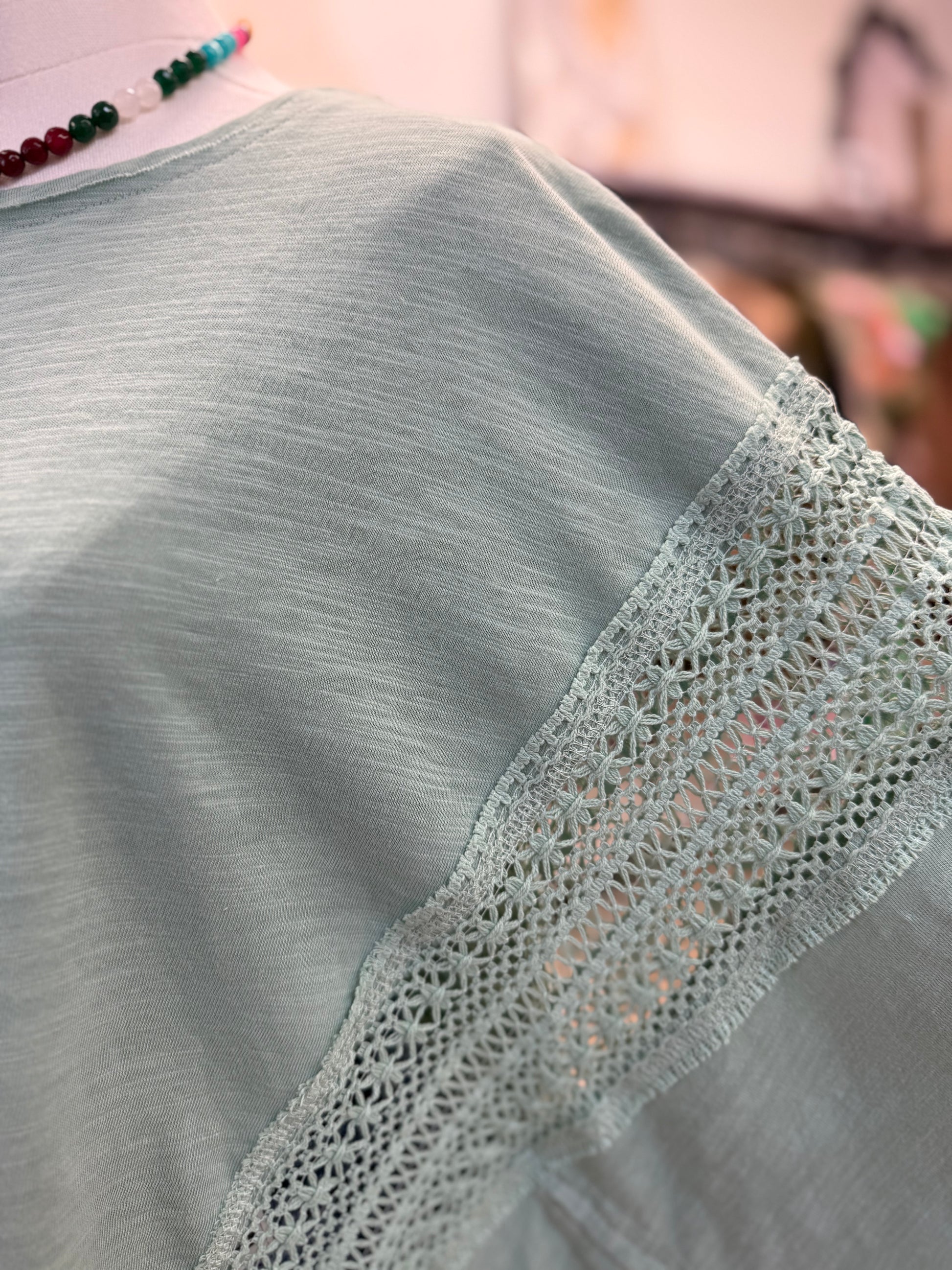 Light teal blouse with lace trim on a blurred background
