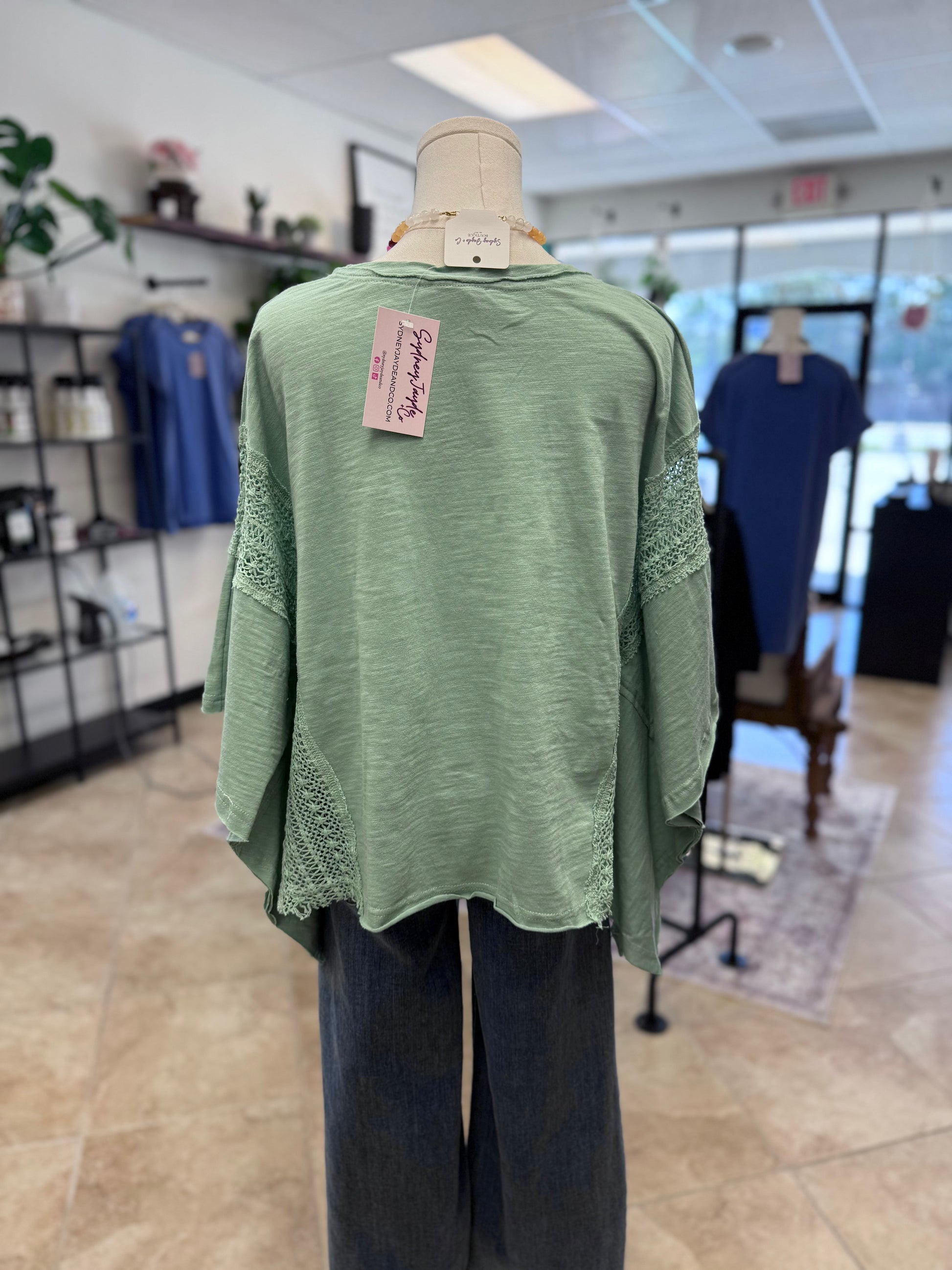 Light teal blouse with lace detail on a mannequin in a store setting with blurred background